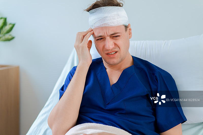 头部缠着纱布绷带的白人男子坐在病床上。图片素材