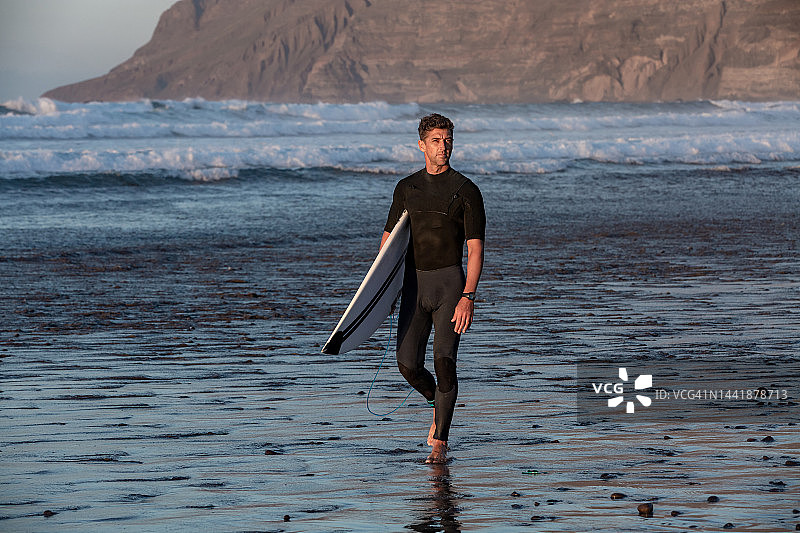 冲浪者沿着海滩行走，滑板上放着冲浪板图片素材