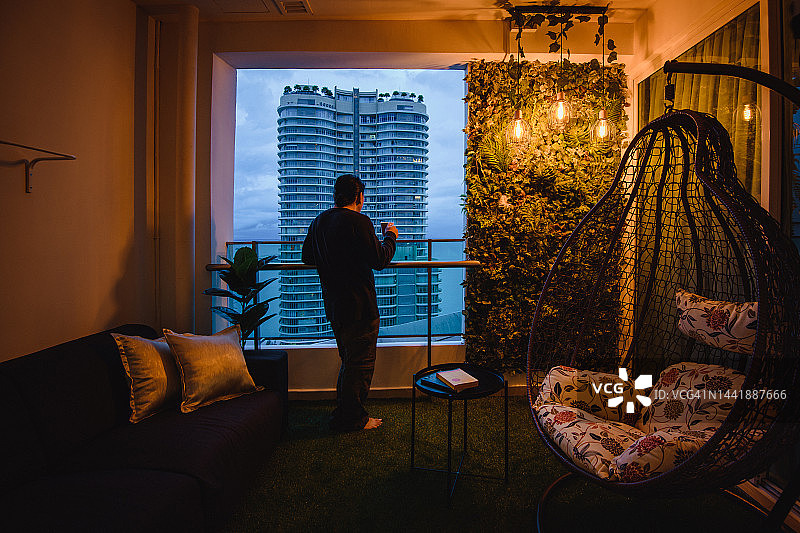 中年男人倚靠在阳台栏杆上，手持咖啡杯图片素材