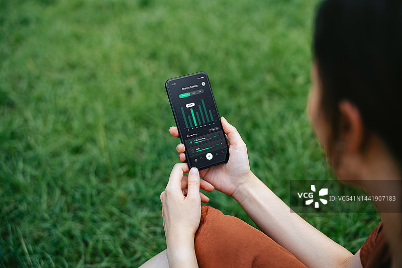 年轻亚洲女性在户外使用智能手机上的智能家居能源监控应用程序图片素材