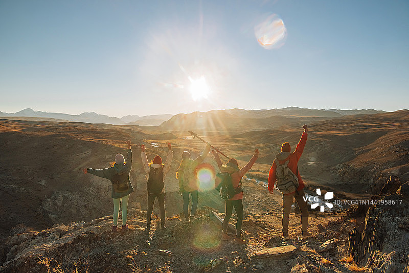 徒步旅行者在山顶日落时分举起手臂庆祝成功图片素材