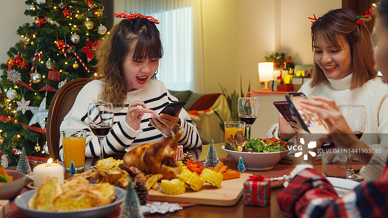 特写：快乐的年轻亚裔女性在餐桌旁拍照，为庆祝节日聚会。图片素材