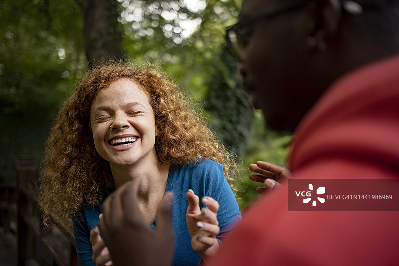在公园里与黑人男性朋友交谈的年轻姜黄色卷发女子图片素材