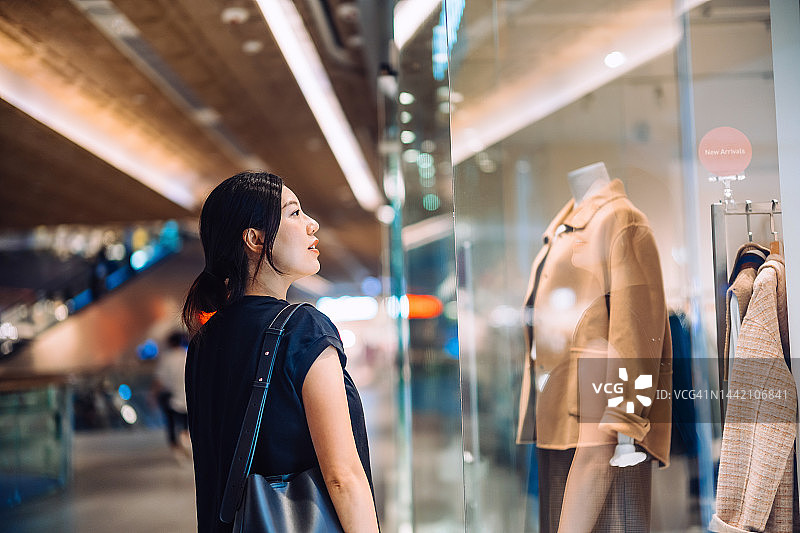 年轻亚洲女性在购物中心精品店外看橱窗展示，享受购物季图片素材