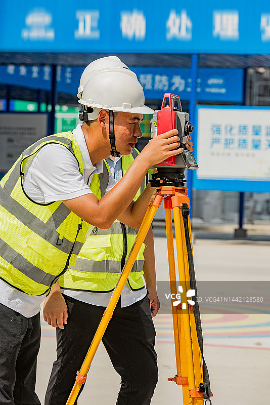 工程师戴白色安全帽，穿黄色背心在建筑工地测量图片素材