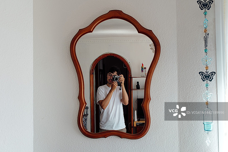 年轻男人用老式相机在镜子前自拍图片素材