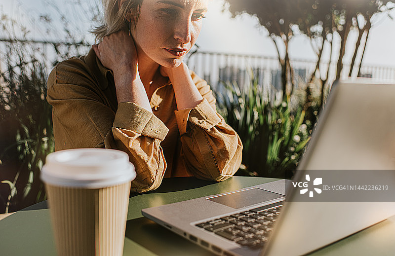 一位女士坐在笔记本电脑前，手扶脖子，看起来压力很大图片素材