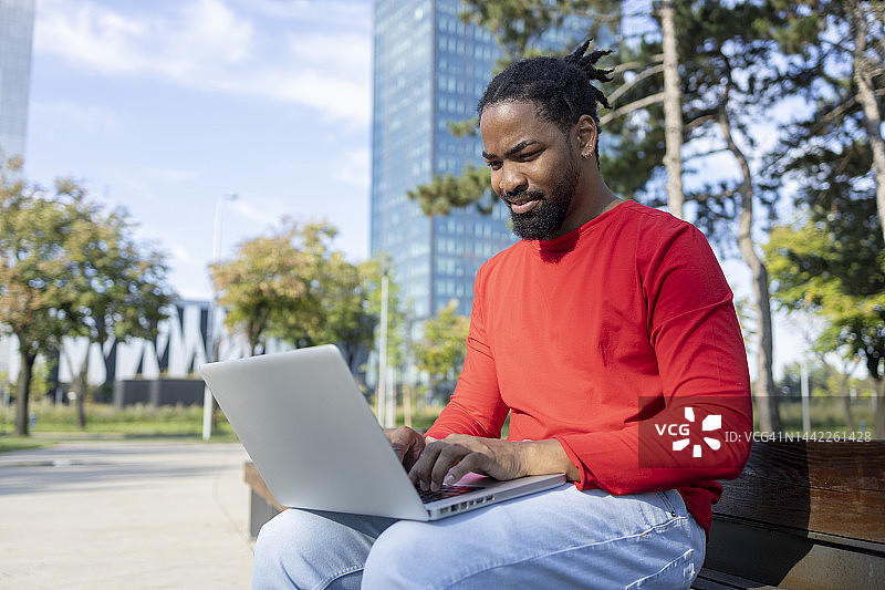 男人在公园长椅上用笔记本电脑工作图片素材