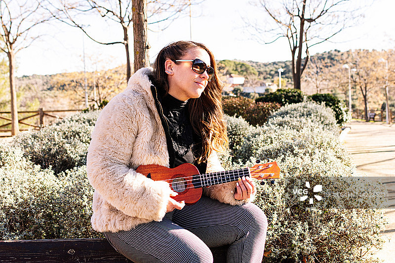 戴着太阳镜在公园里弹尤克里里的年轻女孩图片素材