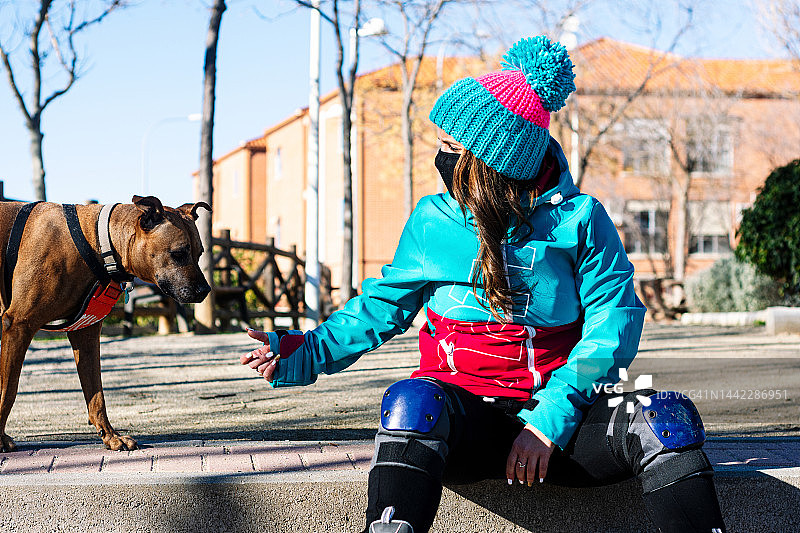戴口罩溜冰女孩和她的狗的肖像。身穿蓝色夹克和蓝色羊毛帽，戴着护膝和溜冰鞋，轮滑概念图片素材
