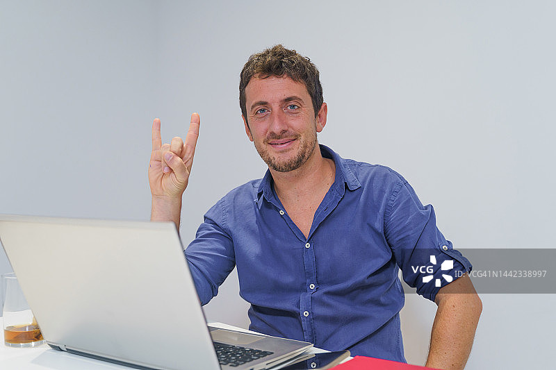 快乐的商人在办公室看着镜头，做出重金属摇滚手势图片素材