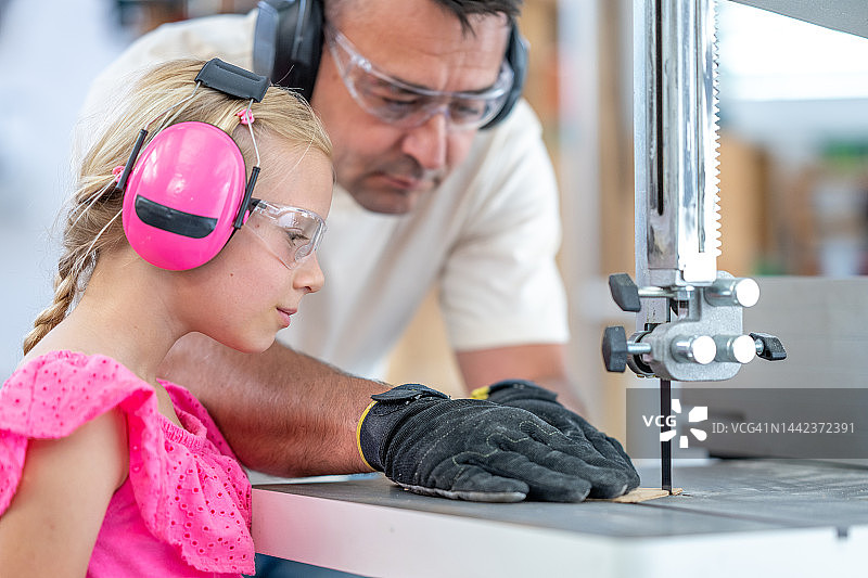 女儿和父亲用电锯切割木材，中景图片素材