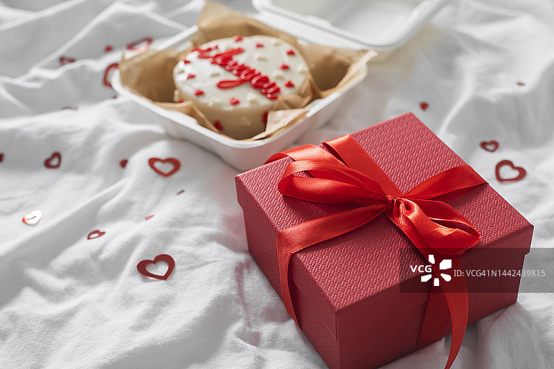情人节礼物：红色礼品盒和白色床单上写着“我爱你”的便当蛋糕图片素材