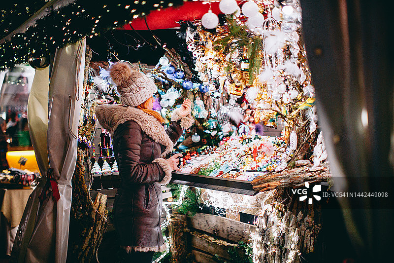 穿着暖和衣服的女人看着灯火通明的圣诞市场摊位图片素材