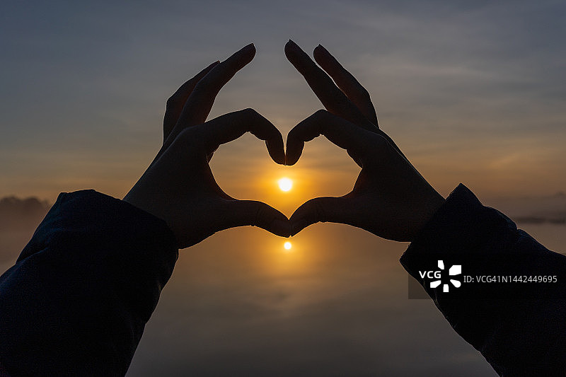 用手做出心形，手中有阳光和水池的倒影图片素材
