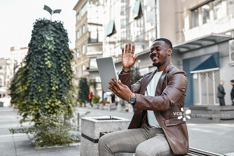 非洲商人坐在欧洲城市的长椅上参加视频会议图片素材