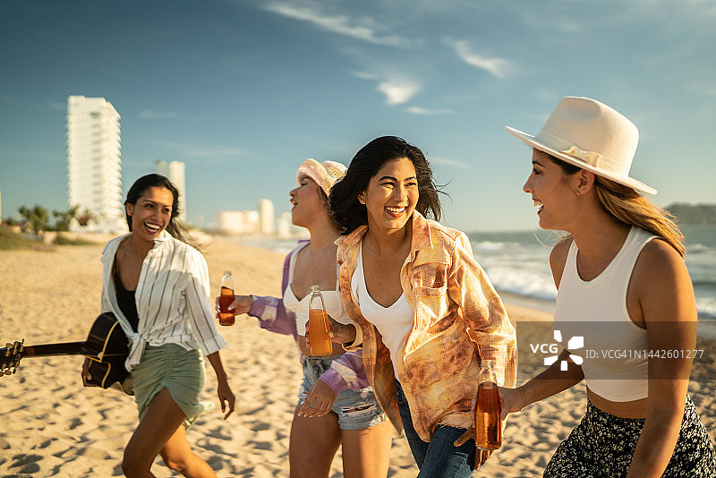 年轻的朋友们带着饮料和吉他在海滩上散步图片素材