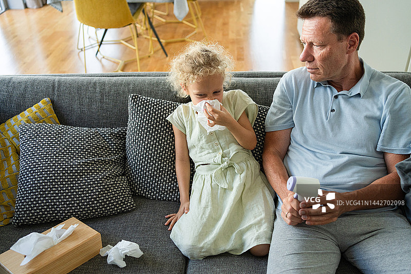 生病的女孩坐在父亲旁边擤鼻涕图片素材