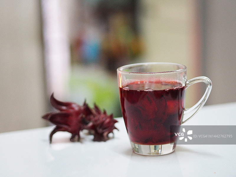 白色桌子上透明玻璃杯中的红色洛神花汁图片素材