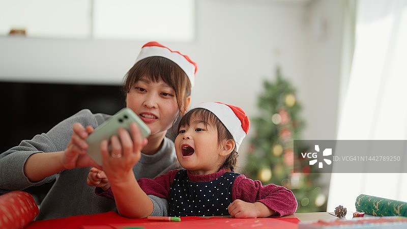 母亲和她上幼儿园的小女儿在家里的客厅里制作圣诞装饰品时拍摄视频和照片图片素材