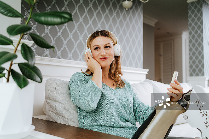 蓝牙耳机连接。快乐的金发女人用腿部假肢，用智能手机听音乐图片素材