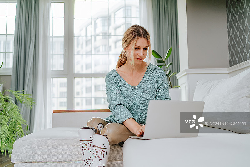 金融和经济商业在线。金发女商人用着人造腿使用笔记本电脑在客厅工作图片素材