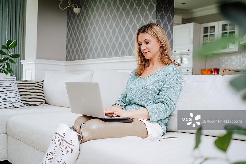 在家玩在线视频游戏。使用笔记本电脑的金发女人，在客厅工作图片素材
