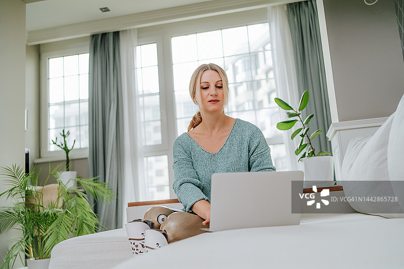 在家工作的自雇女性。使用笔记本电脑的金发女人，装有假肢，低角度视角图片素材
