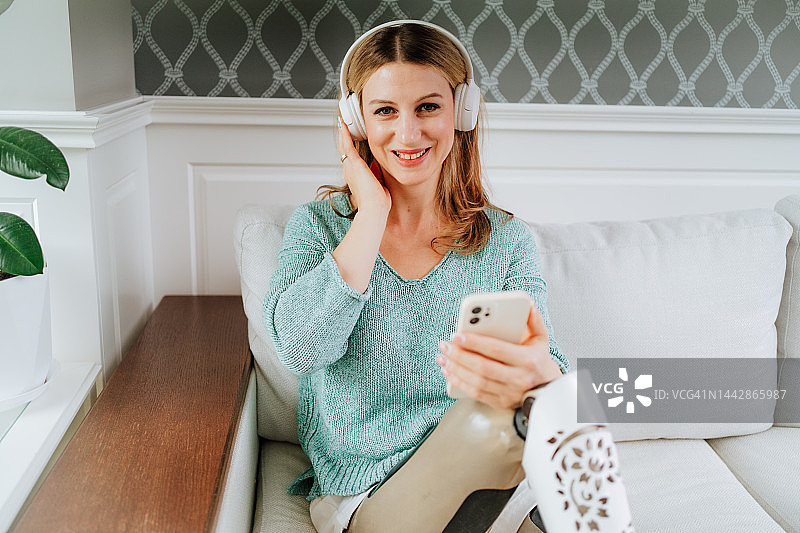 戴着耳机听有声读物，使用手机连接媒体的假肢金发女子图片素材