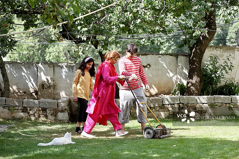 单亲妈妈和两个孩子用割草机修剪自家花园的草坪图片素材