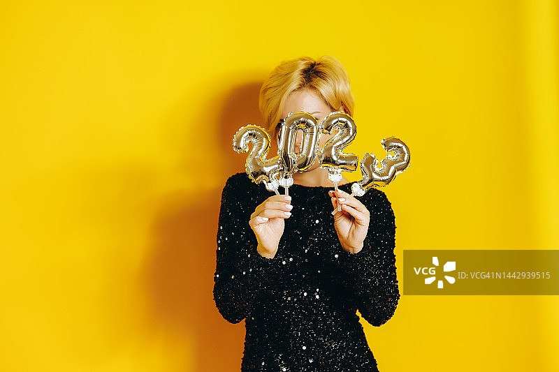 手拿银色2023数字气球躲在后面的黑衣闪亮连衣裙女人图片素材