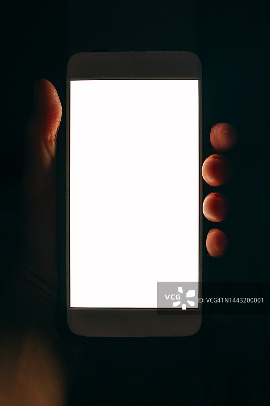 黑暗中人手中的白色屏幕手机图片素材