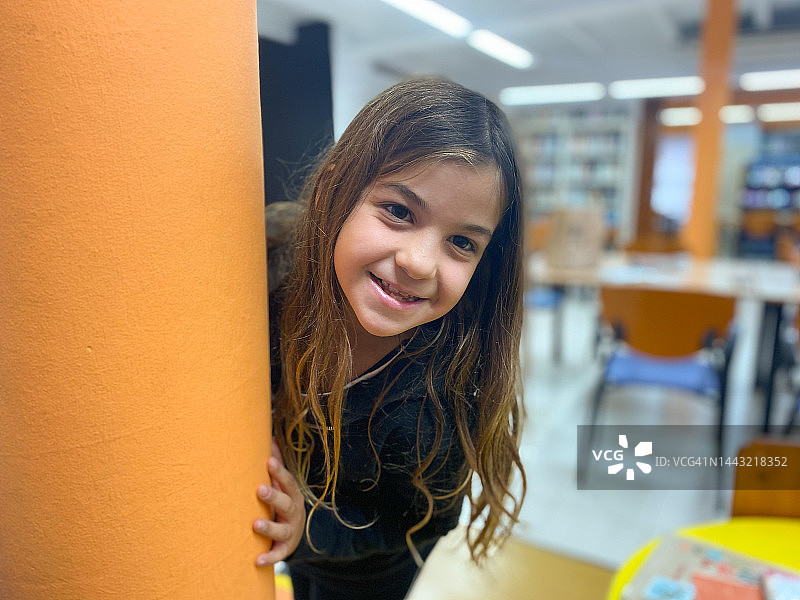 女孩微笑看着从柱子后探出头的相机图片素材