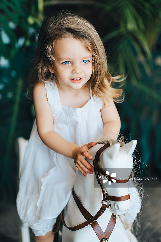 金发小女孩在绿植旁玩摇摇马图片素材