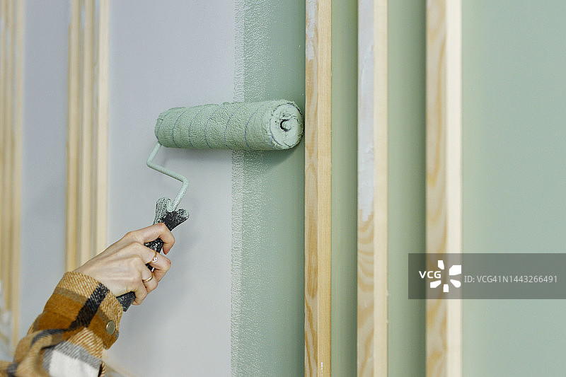 年轻女子在公寓墙上用滚筒刷油漆图片素材