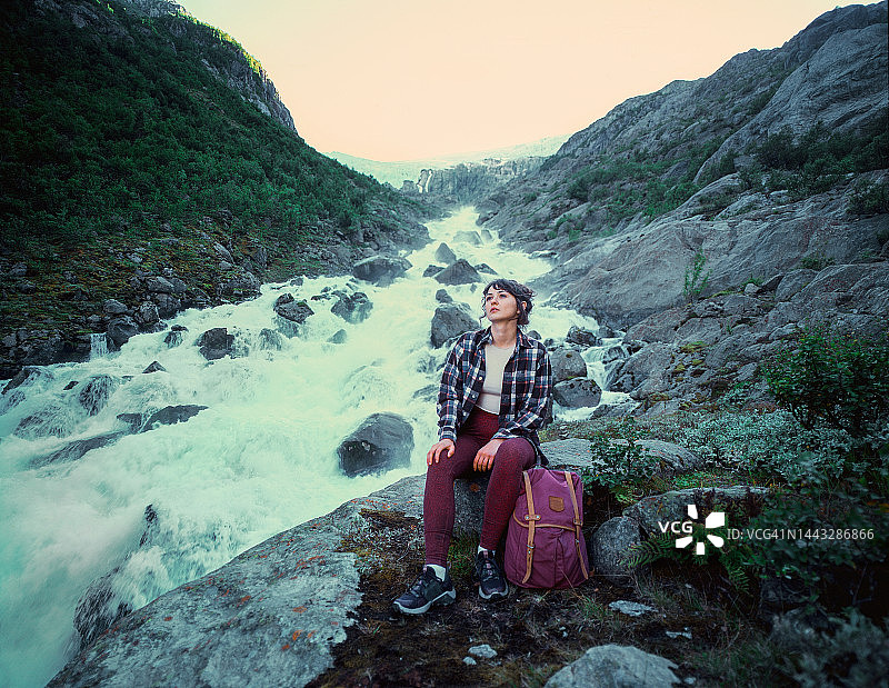 女子坐在河边，背景是约斯特达尔冰川图片素材