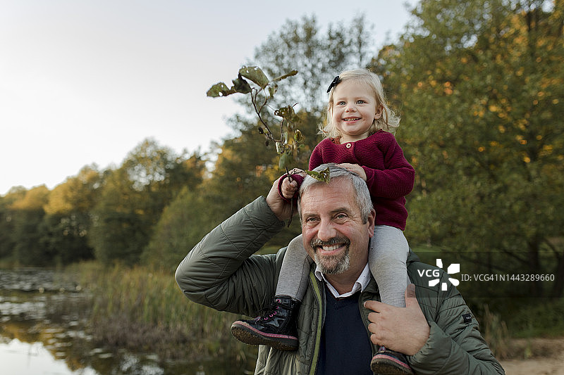 坐在肩膀上拿着植物的微笑男人和孙女图片素材