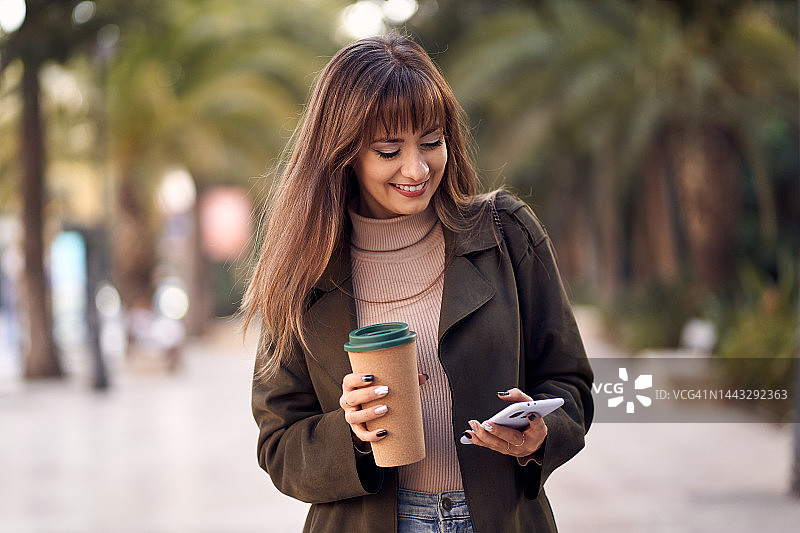 年轻白人女人在街上用手机喝咖啡图片素材