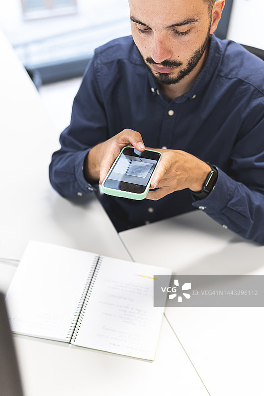 年轻商人用智能手机在办公桌旁拍照图片素材