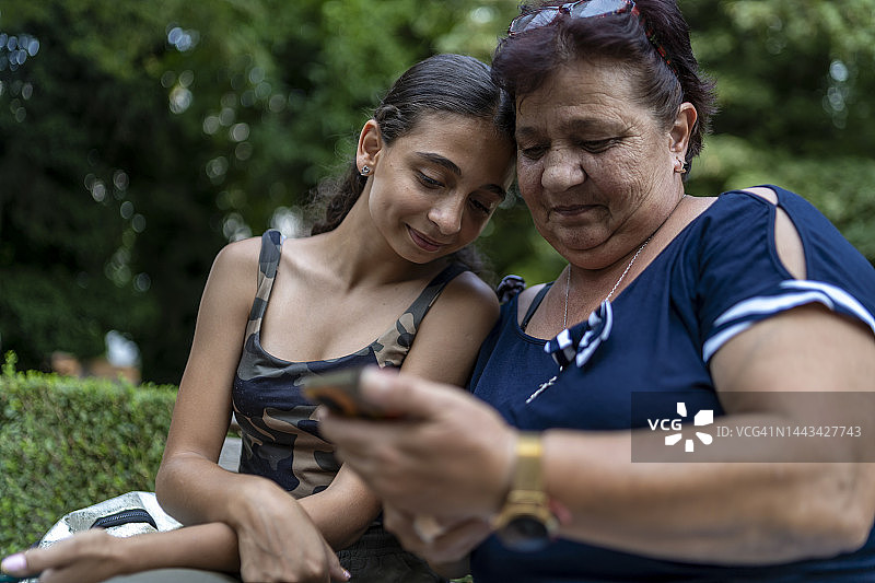 祖母在公园里教奶奶使用智能手机并自拍图片素材