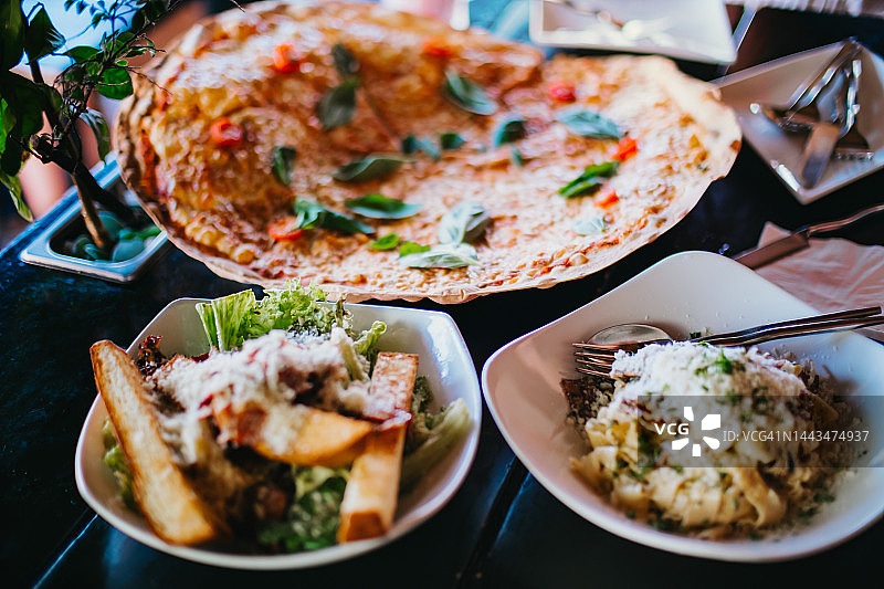 餐厅里新鲜出炉的玛格丽特披萨、凯撒沙拉和培根卡bonara意面图片素材