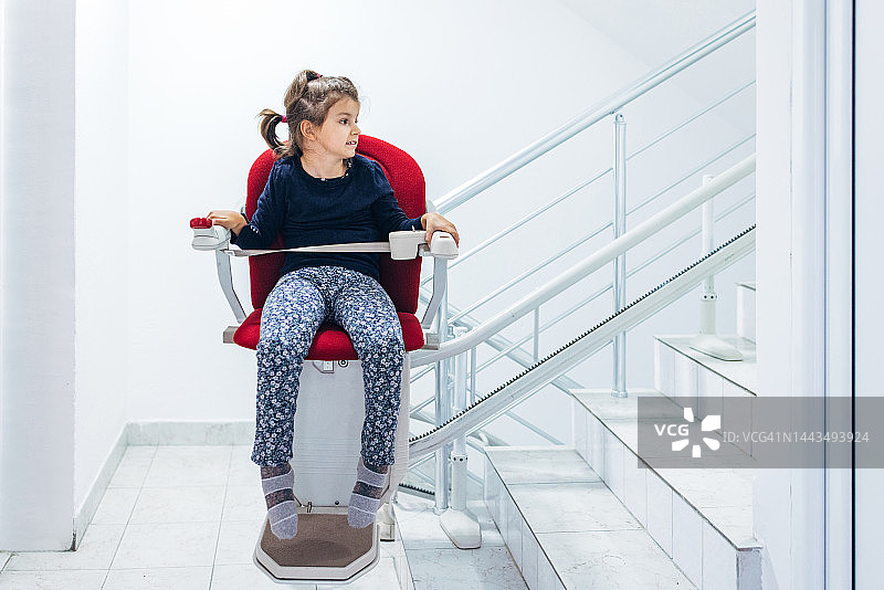 小女孩坐在红色楼梯升降椅上图片素材