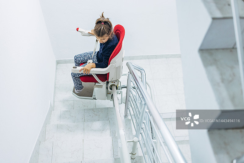 小女孩坐在红色楼梯升降椅上图片素材