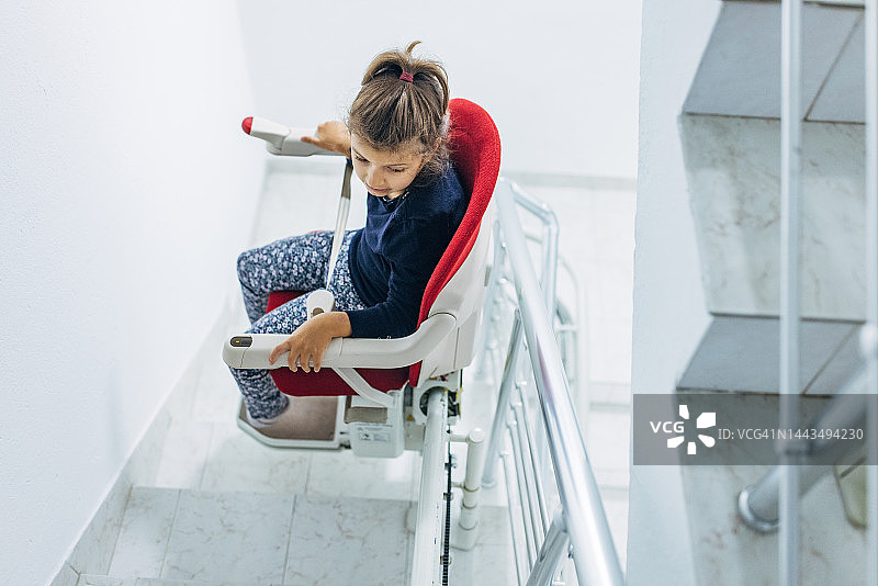 小女孩坐在红色楼梯升降椅上图片素材