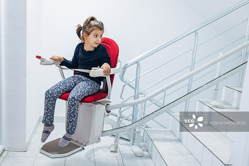 小女孩坐在红色楼梯升降椅上图片素材