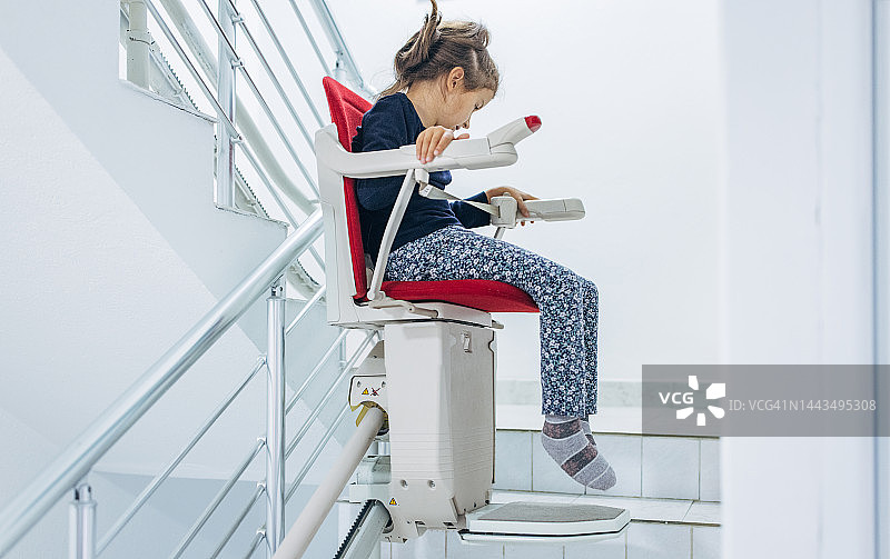 小女孩坐在红色楼梯升降椅上图片素材