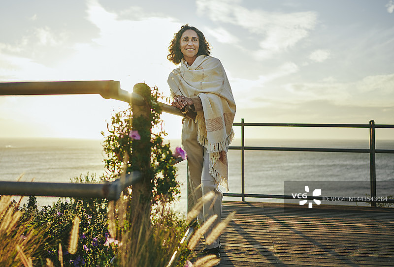 在黄昏时分的海边，眺望远方并微笑的中年妇女图片素材