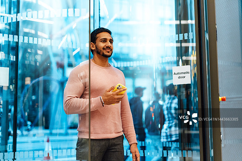 商人手持智能手机进入办公大楼图片素材