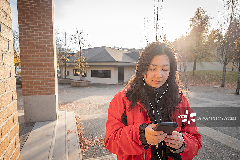 在广场上使用带耳机的智能手机的年轻女子图片素材