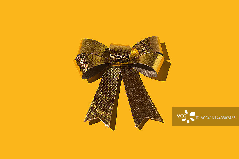 黄色背景上的闪亮金色织物蝴蝶结，圣诞节、庆典、圣诞老人、新年、周年纪念、生日、庆祝和祝贺概念图片素材